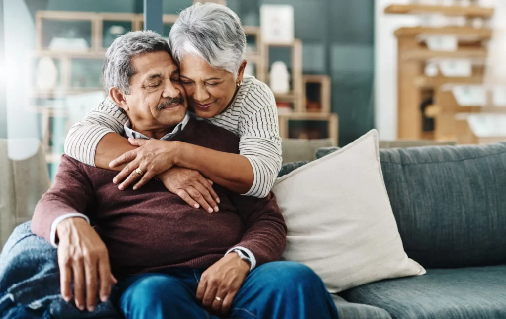 Elderly couple sharing a warm embrace on a cozy couch.
