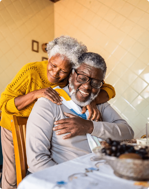 Elderly couple sharing a joyful embrace while sitting at a table.