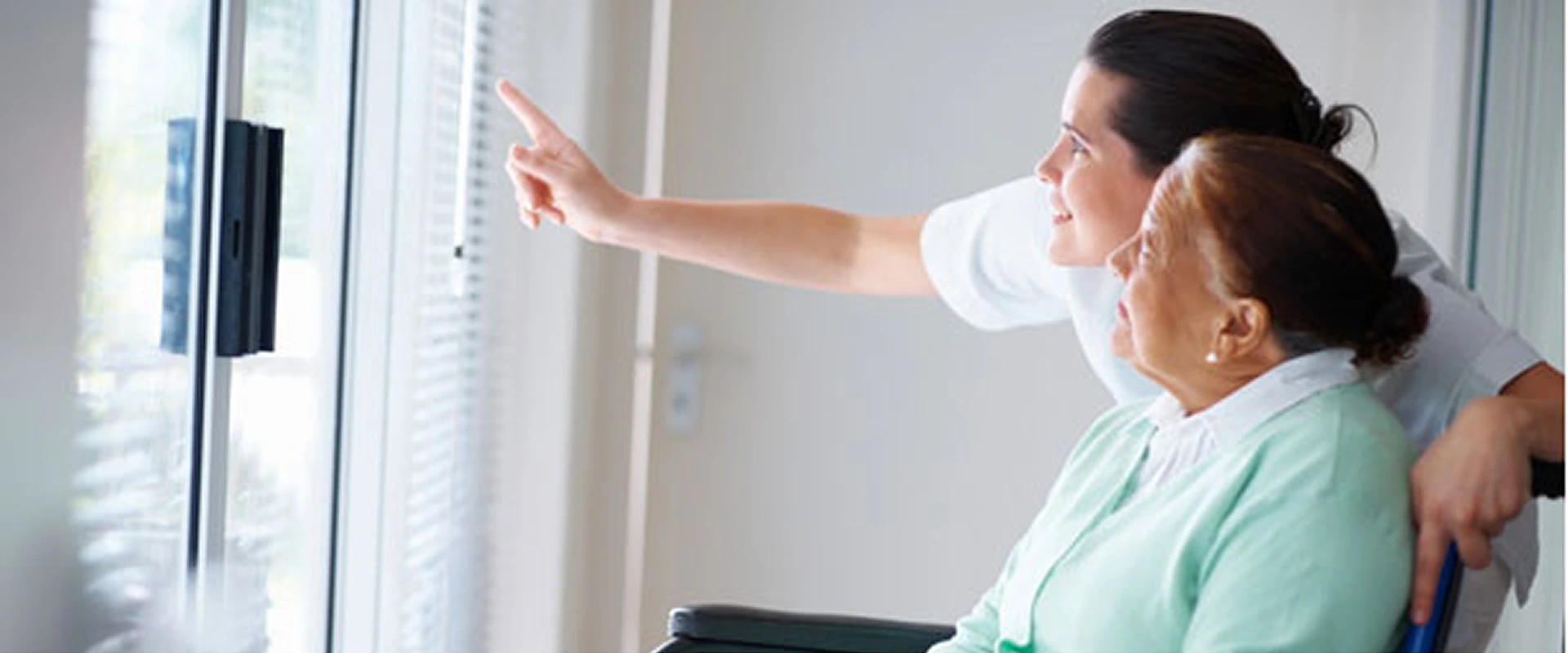 Caregiver assisting elderly woman in wheelchair by pointing at something.