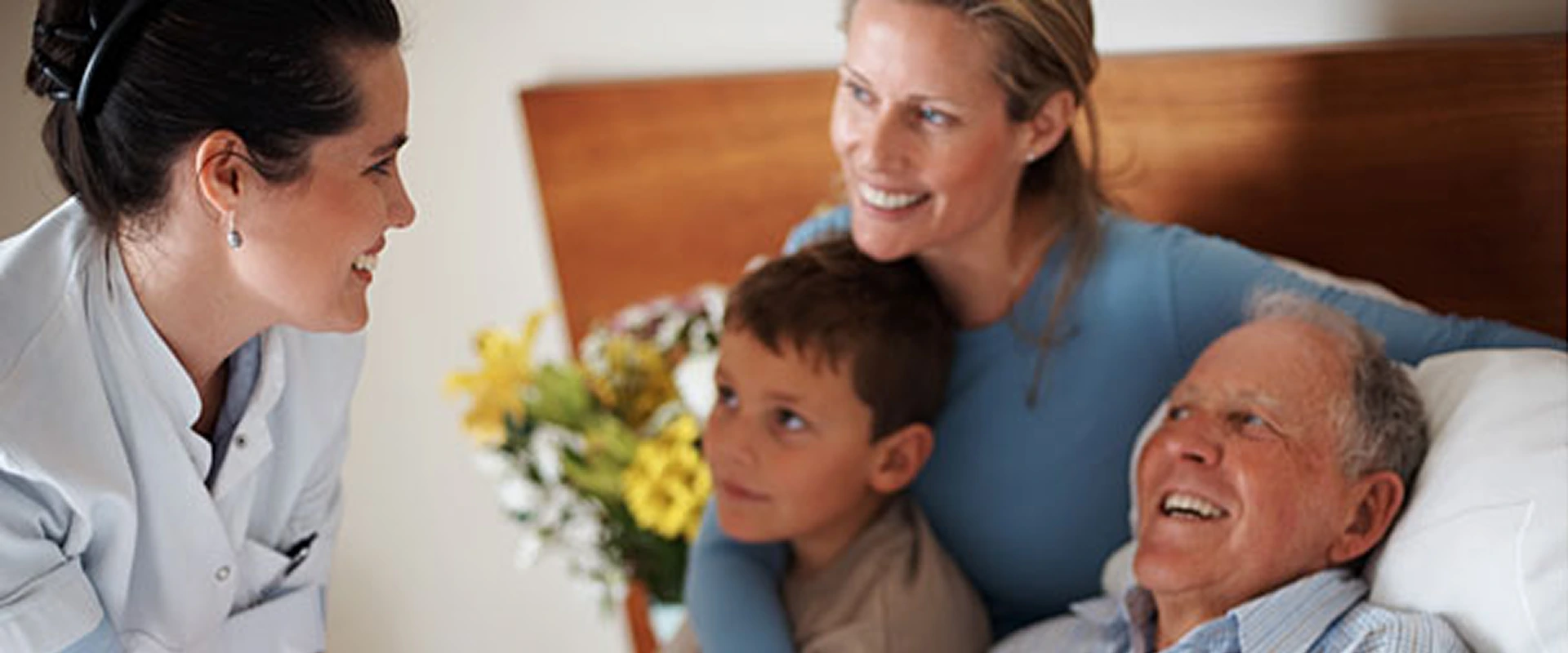 A smiling woman embracing a young boy with flowers in the background.