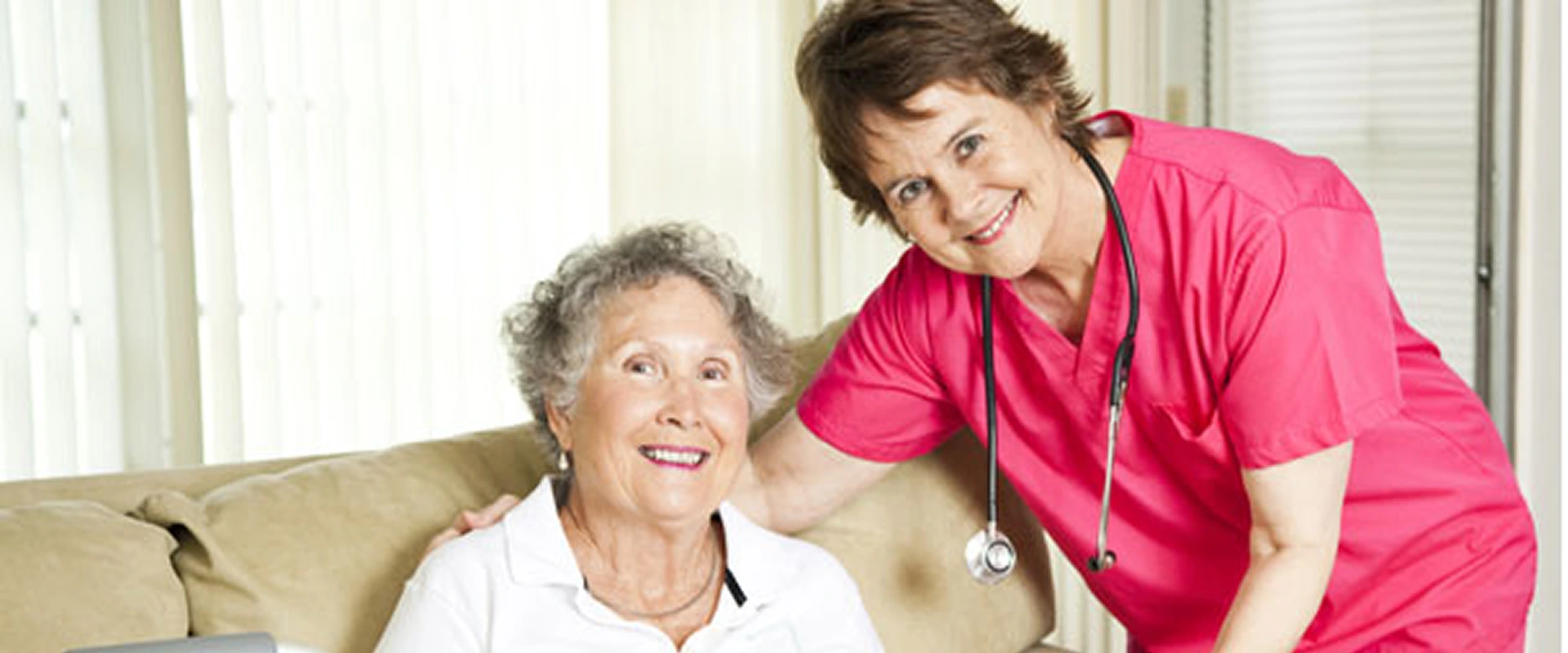 Smiling elderly woman with a caring nurse beside her.